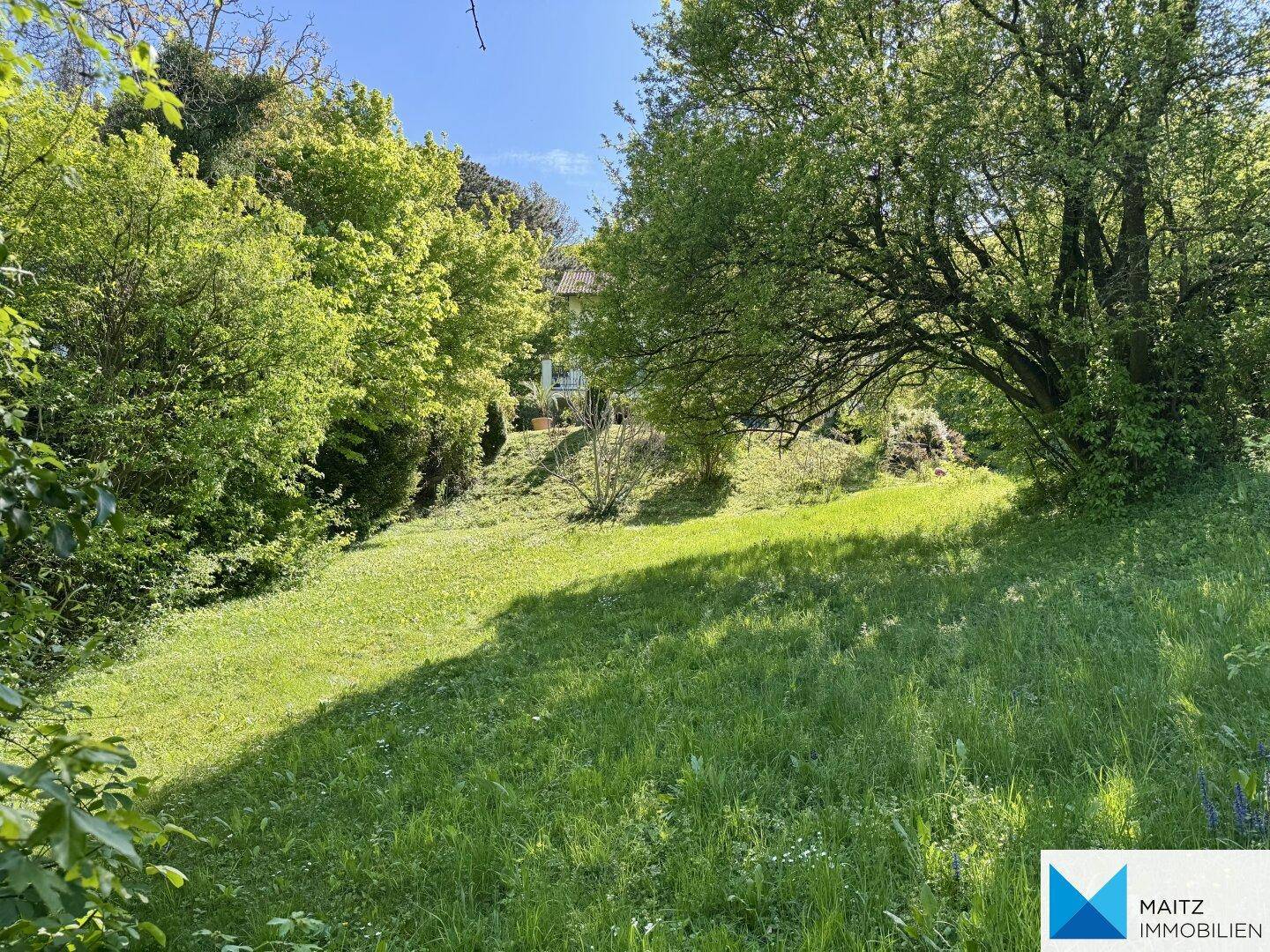 Grüne, leicht abfallende Gartenfläche mit Bäumen und Blick auf die umliegende Wohnbebauung.