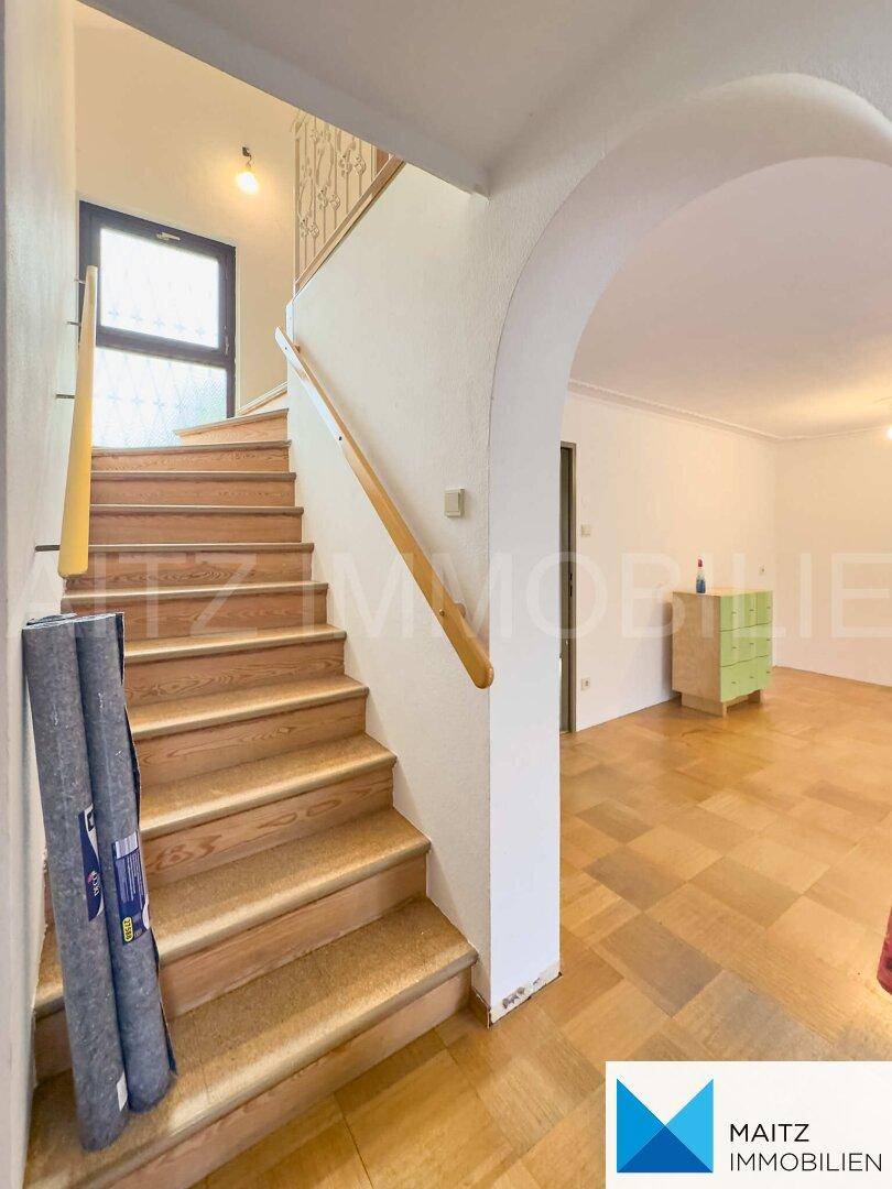 Holztreppe mit Handlauf führt in die obere Etage, angrenzend an einen hellen Flurbereich.