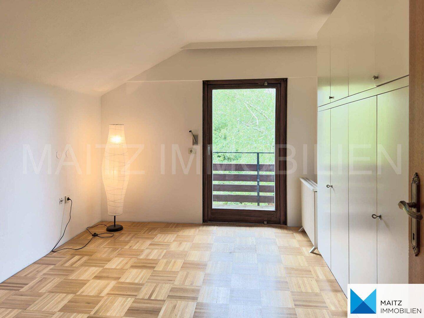 Helles Zimmer mit Parkettboden, Einbauschränken und Zugang zu einem kleinen Balkon mit Grünblick.