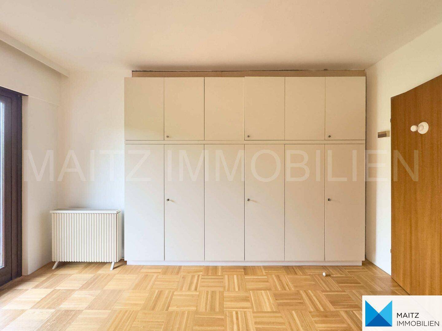 Praktische Einbauschränke bieten viel Stauraum in diesem hellen Zimmer mit Parkettboden.