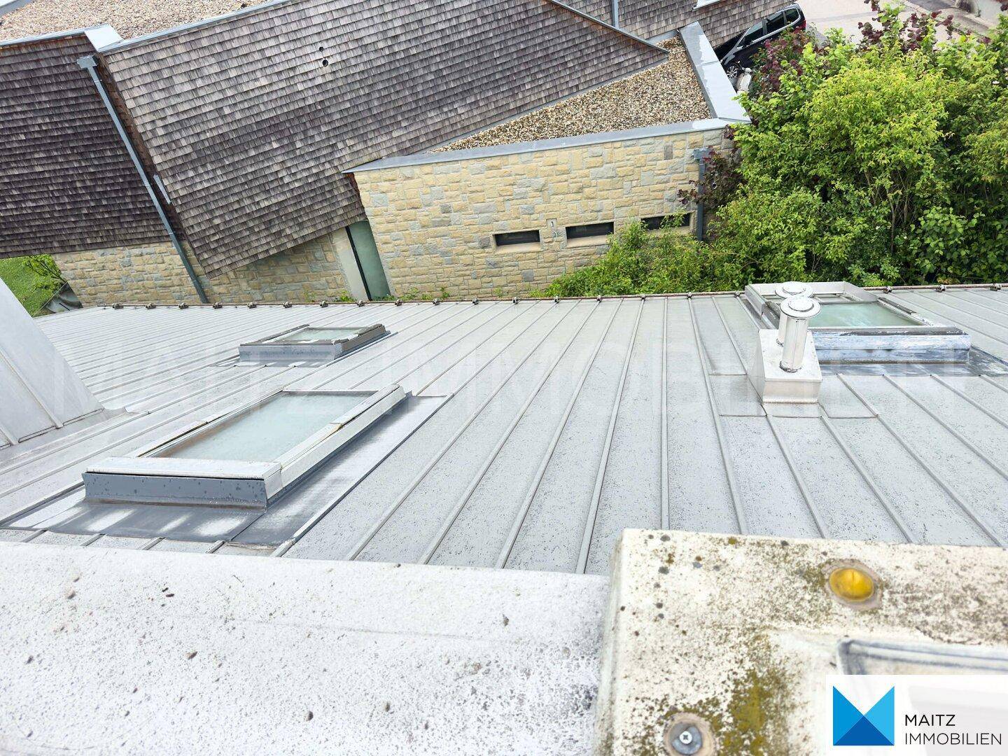 Metallgedecktes Dach mit Dachfenstern und Blick auf angrenzende Gebäude mit unterschiedlichen Dachformen.