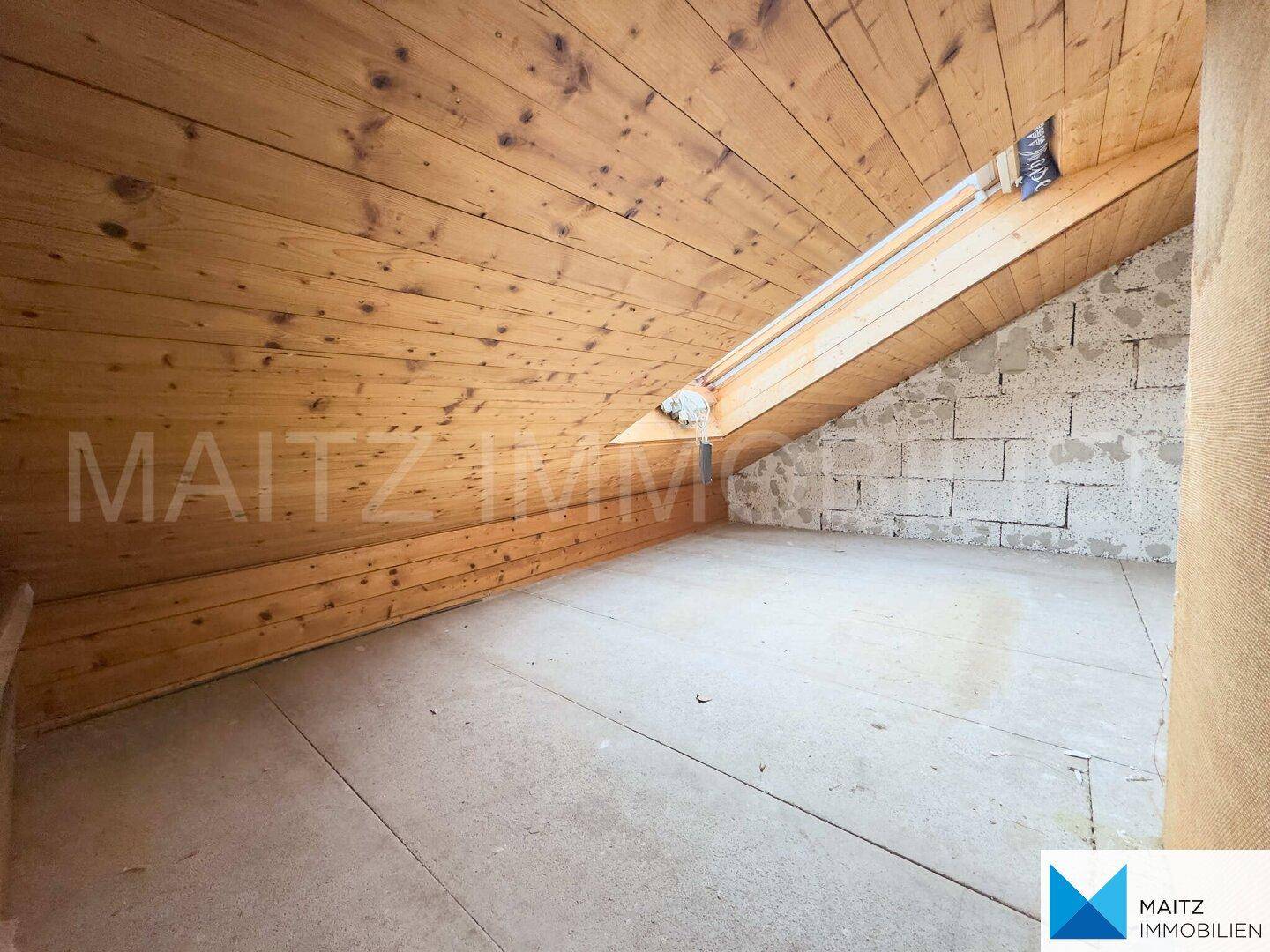 Ausbaufähiger Dachbodenbereich mit sichtbaren Holzdeckenbalken und unfertigen Wänden.