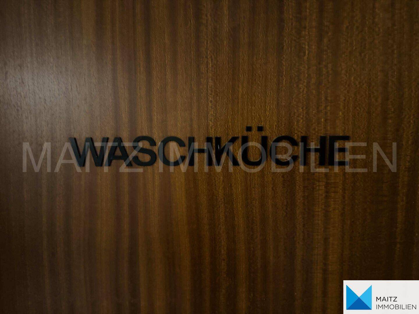 Holztür mit der Aufschrift 'Waschküche', weist auf den Gemeinschaftswaschraum hin.
