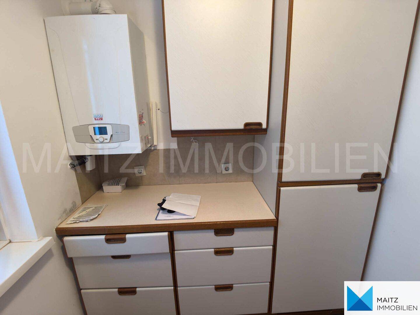 Küchenbereich mit weiteren Schränken, Arbeitsfläche und Warmwasserboiler, gut organisiert.