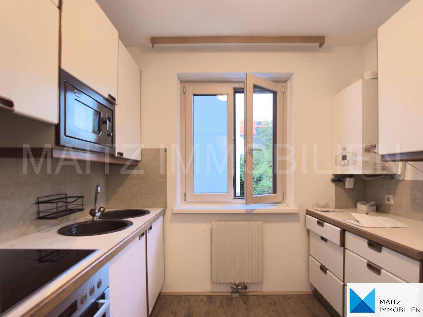 Funktionale Küche mit weißen Schränken, Holzarbeitsplatte, Spüle und Fenster für Tageslicht.