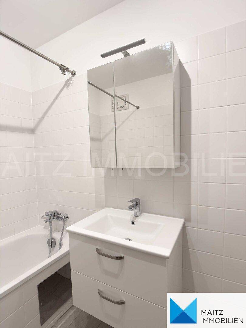 Detailansicht des Badezimmers mit modernem Waschbecken, Spiegelschrank und weißen Wandfliesen.