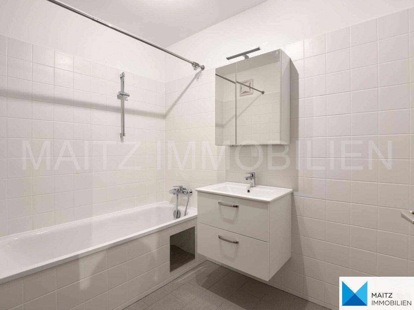 Modernes Badezimmer mit weißen Fliesen, Badewanne, Waschbecken und Spiegelschrank.