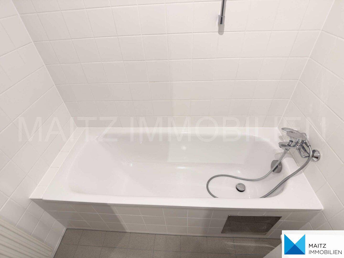 Badewanne in weiß gefliestem Badezimmer, sauber und funktional, bereit zur Nutzung.