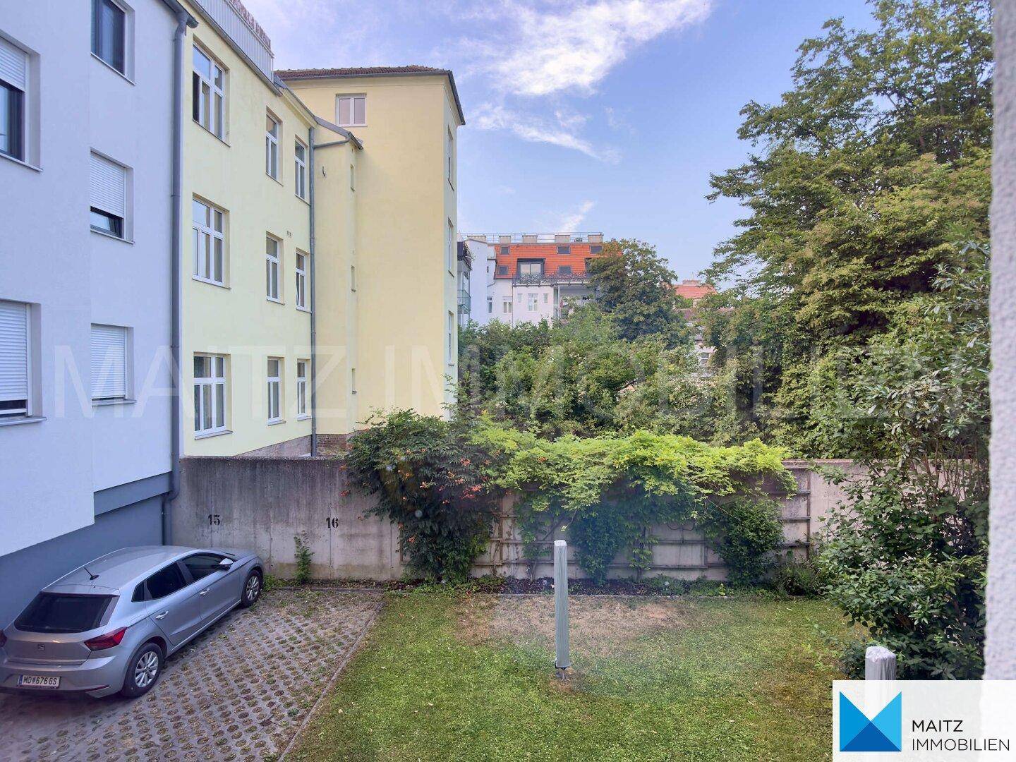 Blick auf den Innenhof mit Parkplatz, Grünfläche und umliegenden Gebäuden.