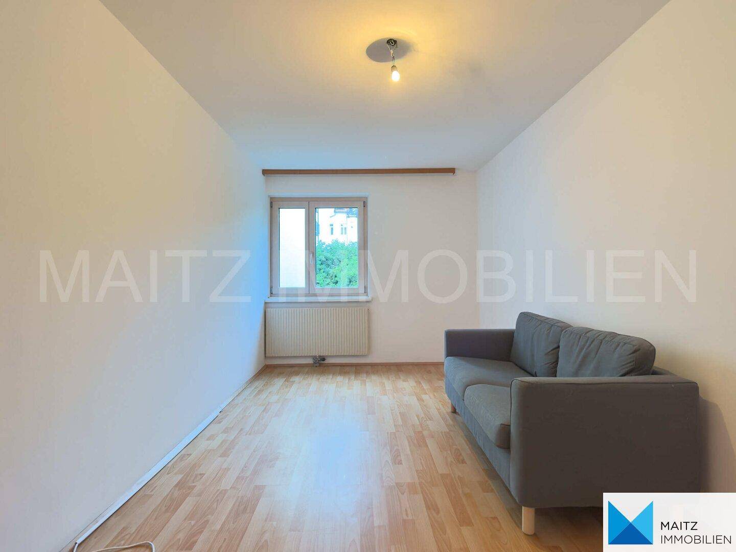 Gemütliches Wohnzimmer mit Sofa, Parkettboden und einem Fenster, hell und einladend.