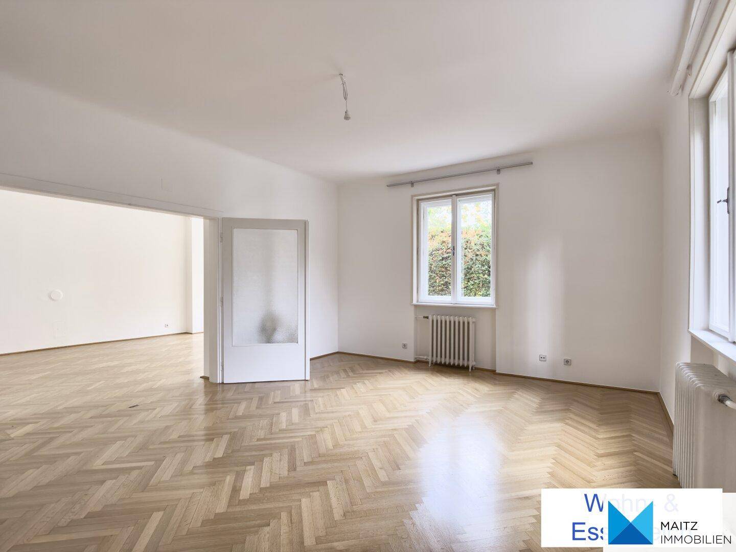 Lichtdurchfluteter Raum mit Fischgrätparkett und einem Fenster, das viel Tageslicht hereinlässt.