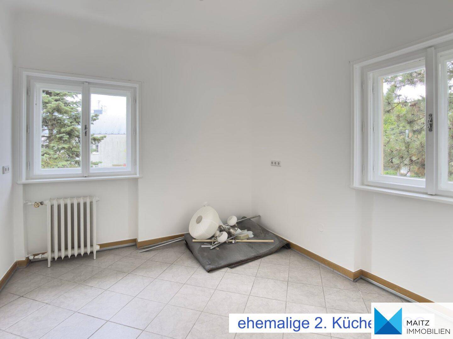 Ehemalige Küche oder Hauswirtschaftsraum mit Fliesenboden und zwei Fenstern.