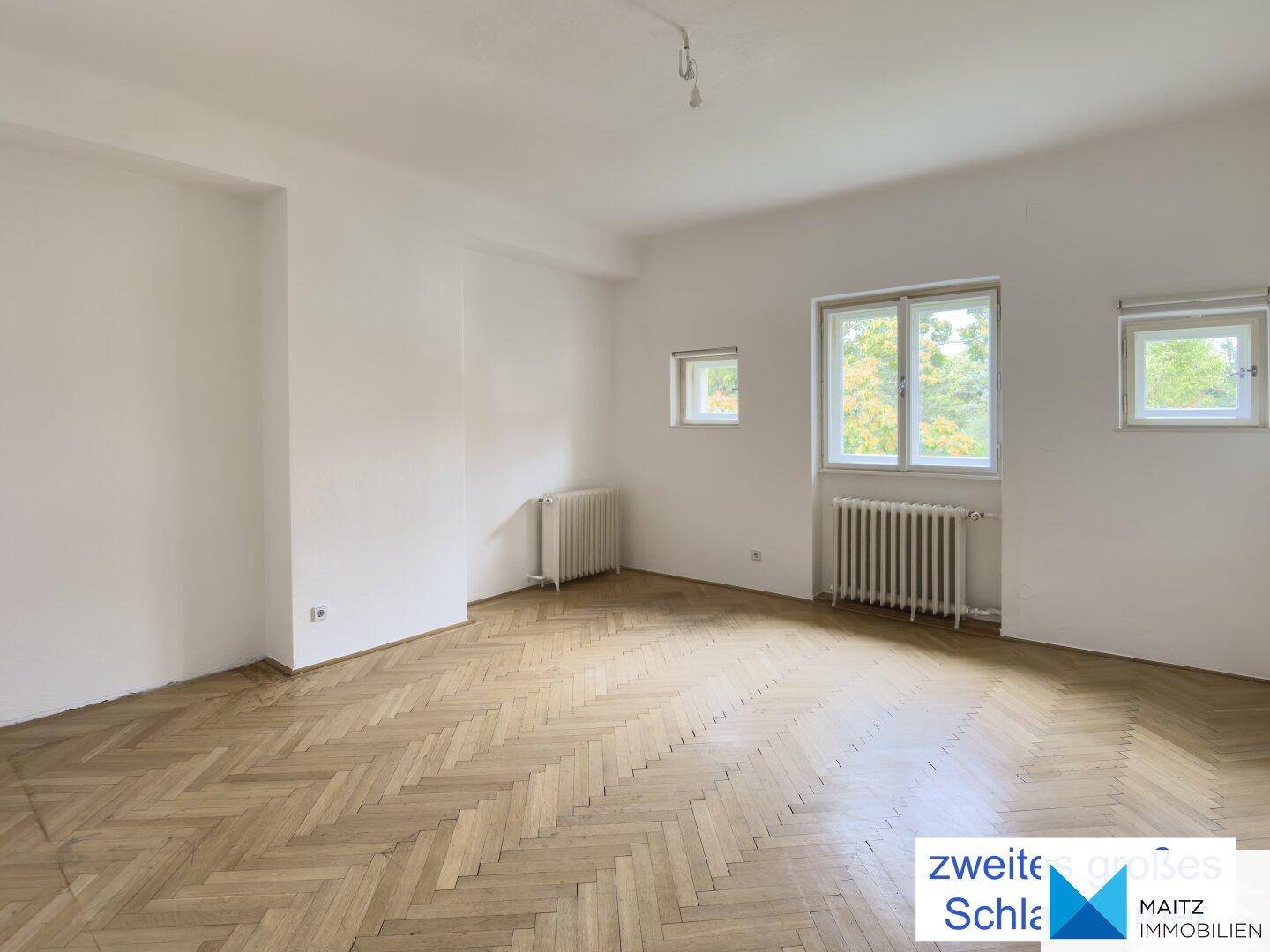 Zweites großes Schlafzimmer mit Fischgrätparkett und hellen Wänden.