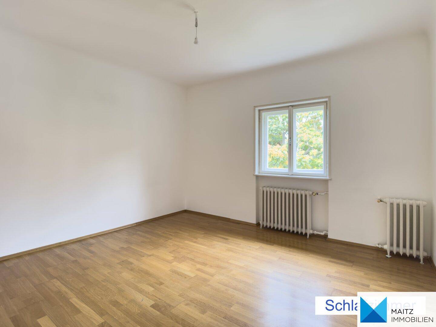 Helles Schlafzimmer mit Holzfußboden und einem Fenster, das den Raum erhellt.