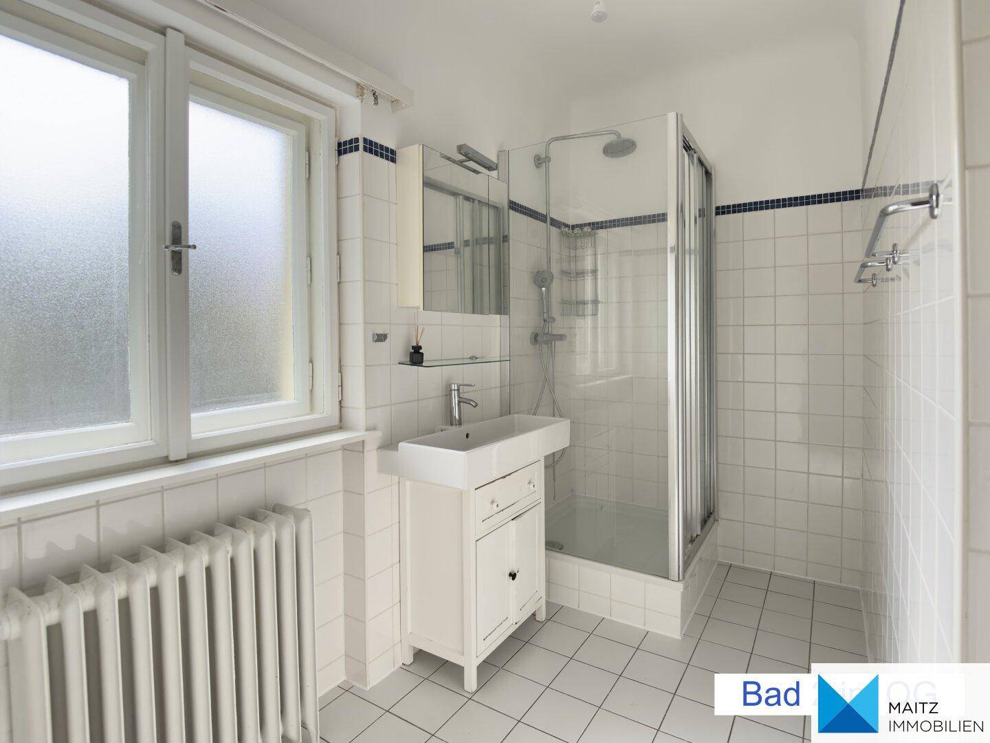Modernes Badezimmer mit weißen Fliesen, Duschkabine und einem Waschbecken.