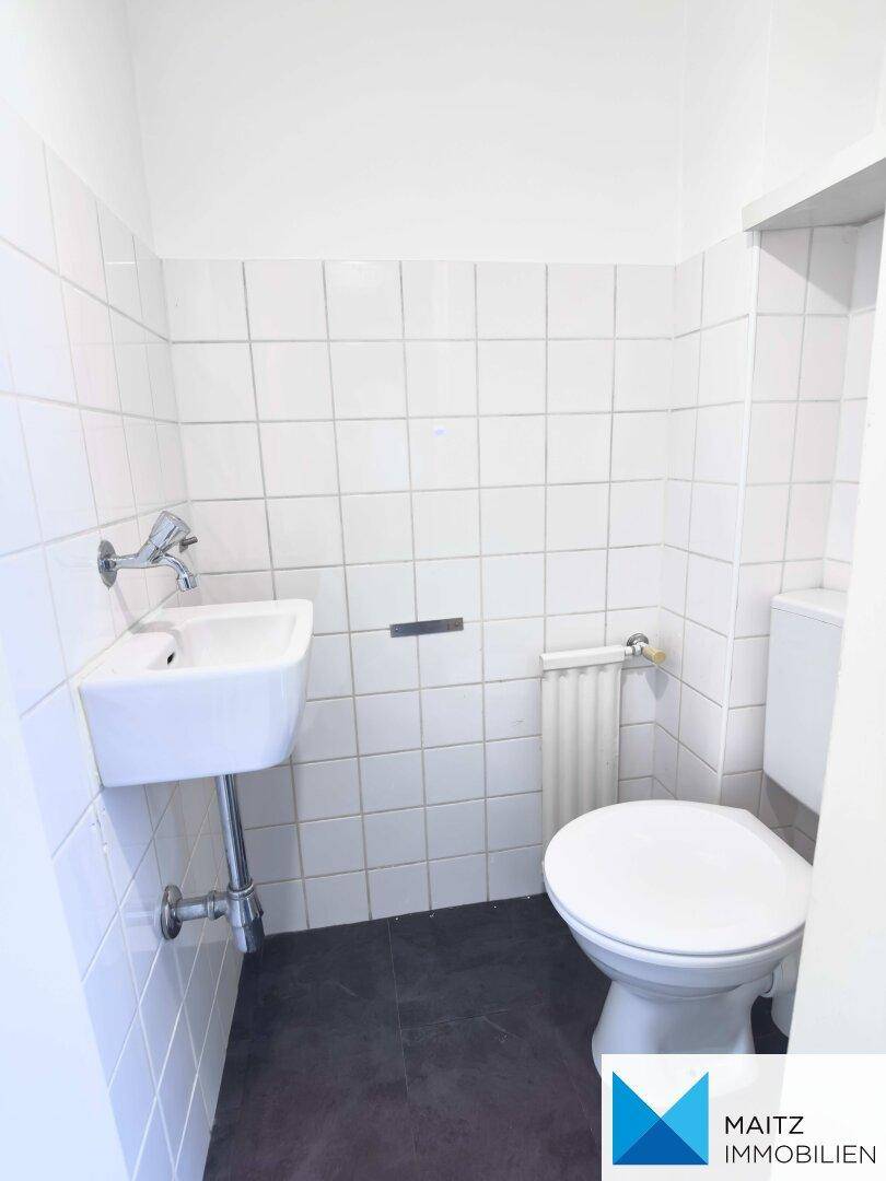 Kleines Gäste-WC mit weißen Fliesen, Toilette und einem kompakten Waschbecken.
