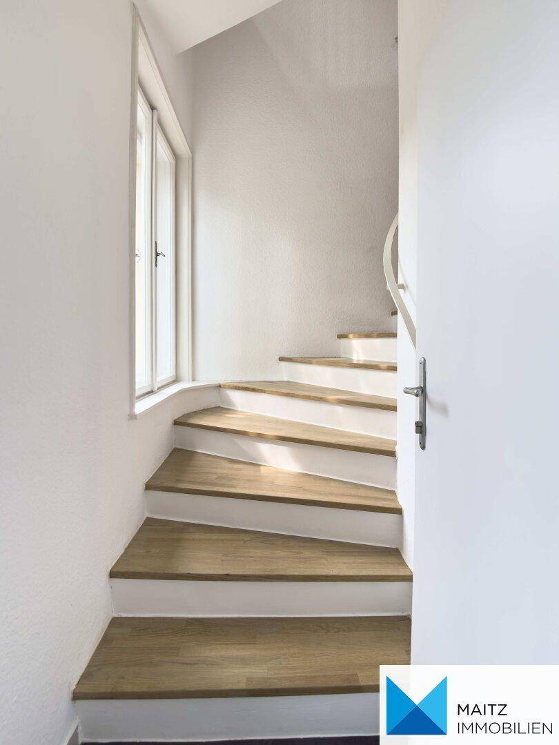 Elegante Holztreppe mit weißen Setzstufen, die in die obere Etage führt.