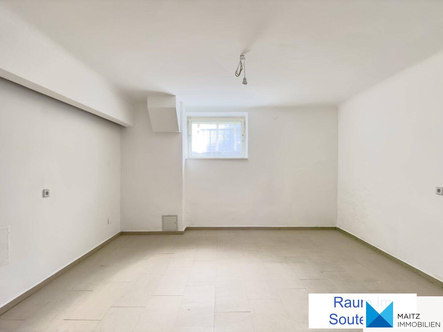 Heller Raum im Untergeschoss mit weiß gestrichenen Wänden und einem kleinen Fenster.