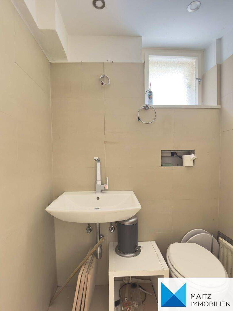 Modernes Gäste-WC mit hellem Fliesenboden, Waschbecken und einem kleinen Fenster.