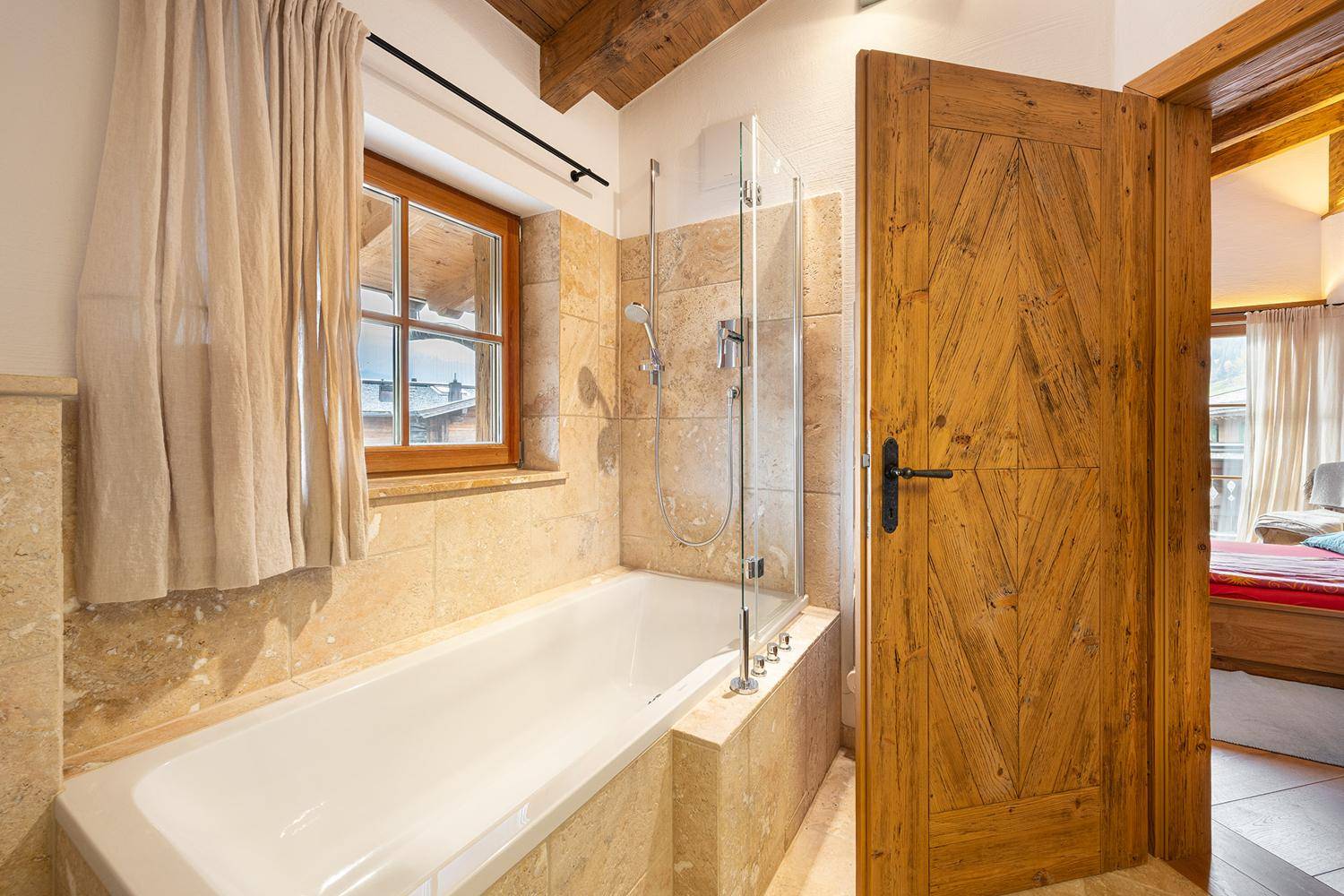 Helles Badezimmer mit Badewanne, Fenster und Natursteinfliesen, direkt vom Schlafzimmer zugänglich.
