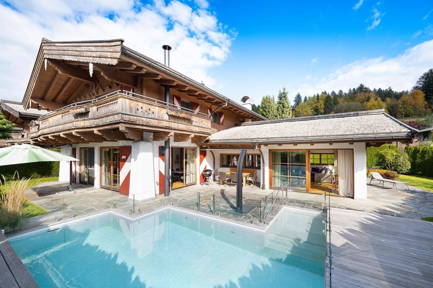 Traditionelles Chalet mit großem Außenpool, Holzfassade und Bergblick unter blauem Himmel.