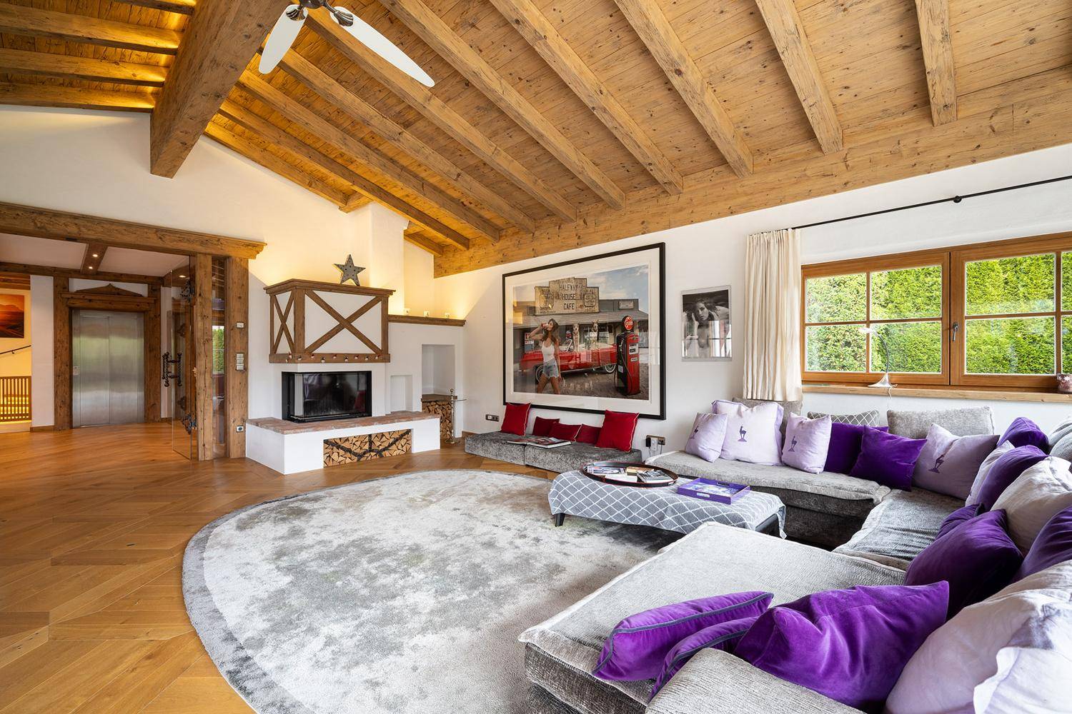 Gemütliches Wohnzimmer mit Holzbalkendecke, Kamin und großem Sofa, hell und einladend.