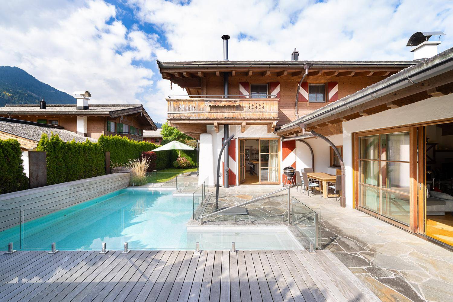 Chalet-Stil Haus mit Außenpool, Holzterrasse und Bergblick unter blauem Himmel.