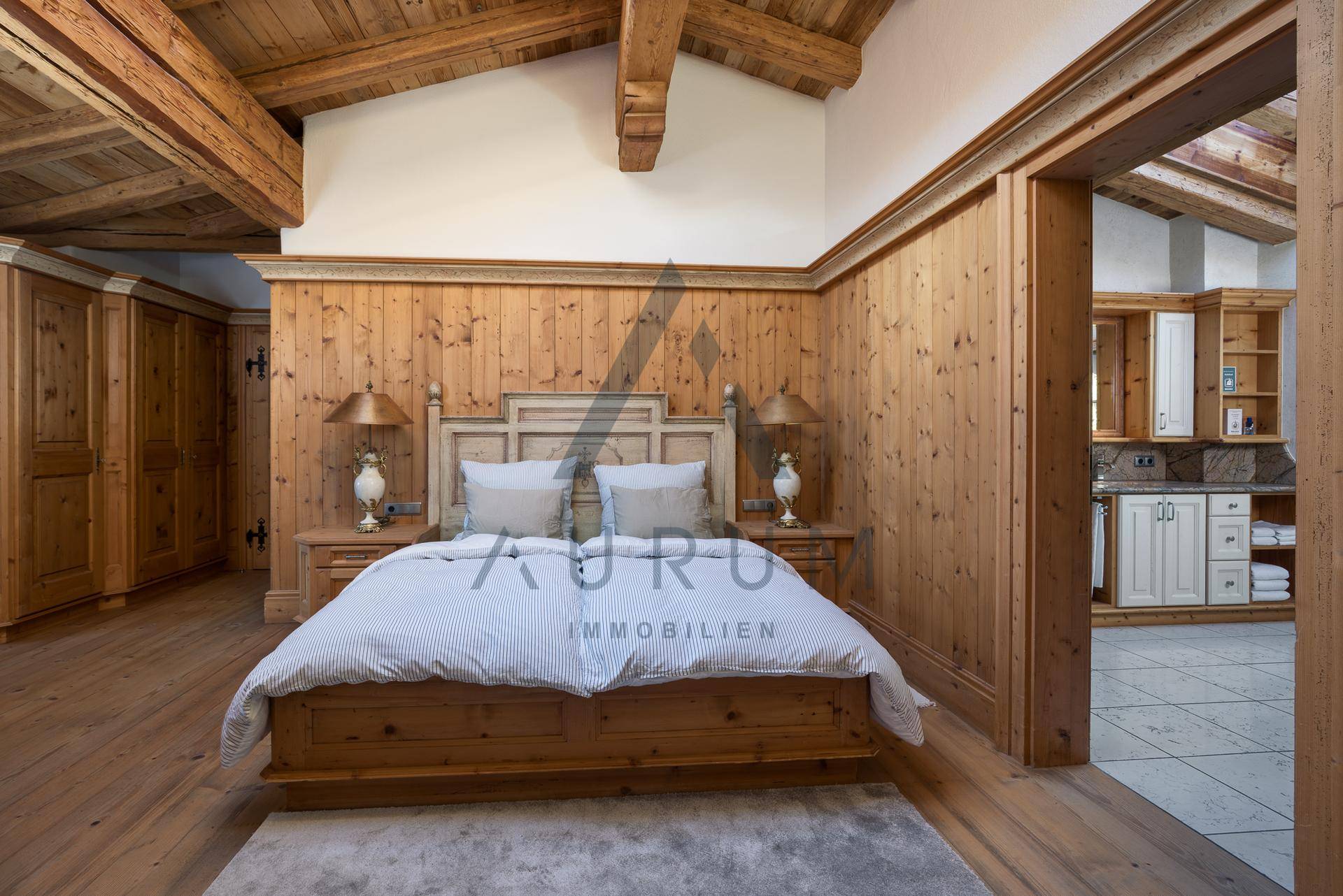 Gemütliches Schlafzimmer mit viel Holz, Holzbalkendecke und Zugang zu einem weiteren Raum.