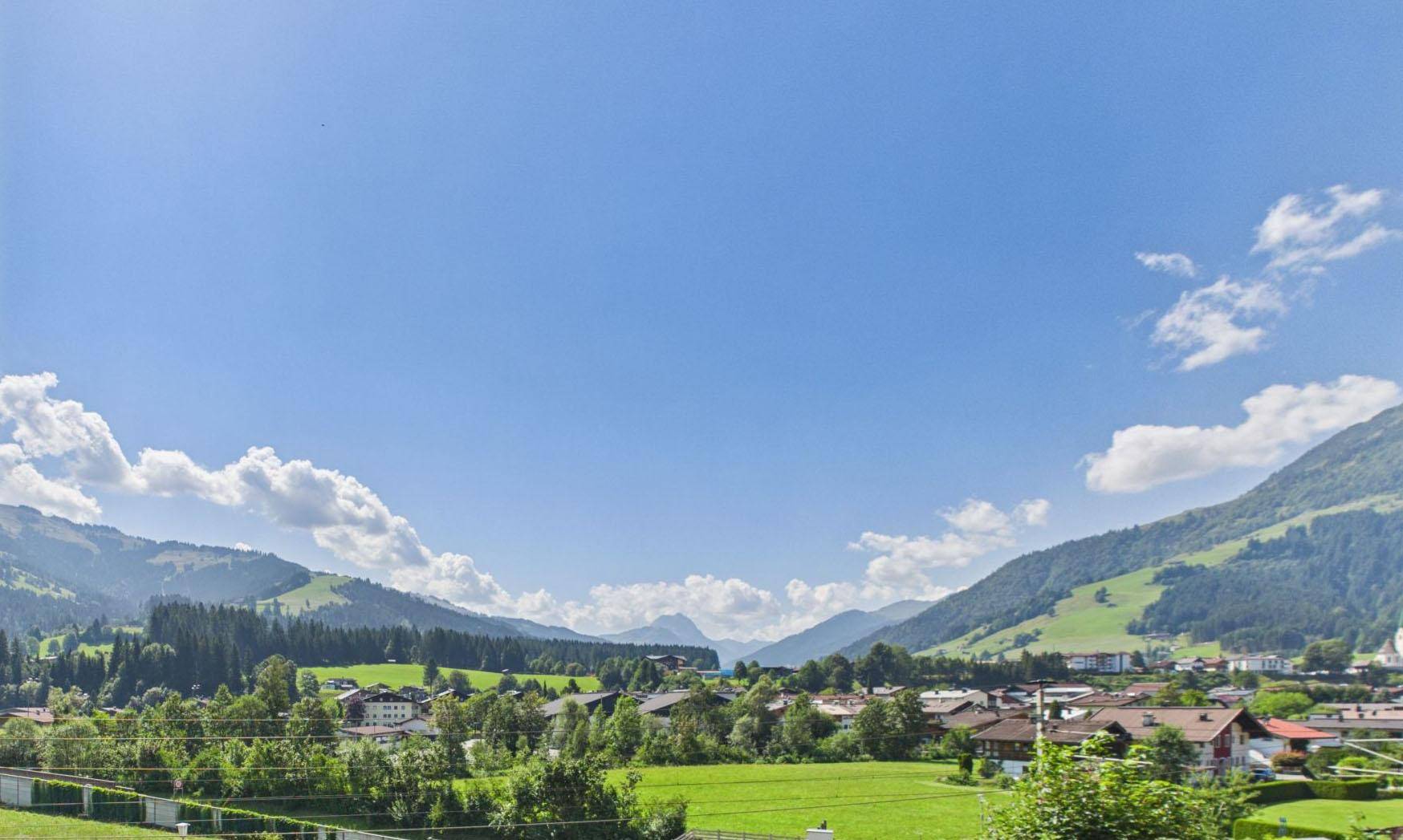 Panoramablick über ein grünes Tal mit Dorf und majestätischen Bergen im Hintergrund.