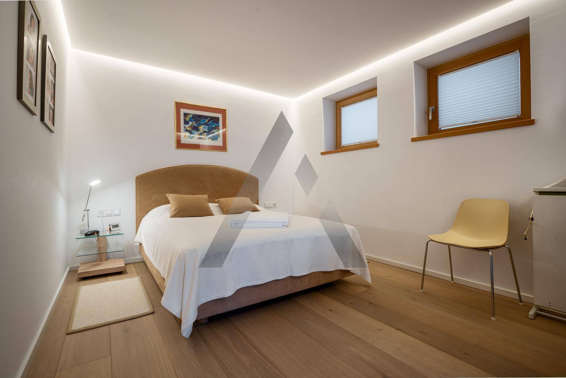 Ruhiges Schlafzimmer mit Doppelbett und zwei kleinen Fenstern, ausgestattet mit Holzfußboden.