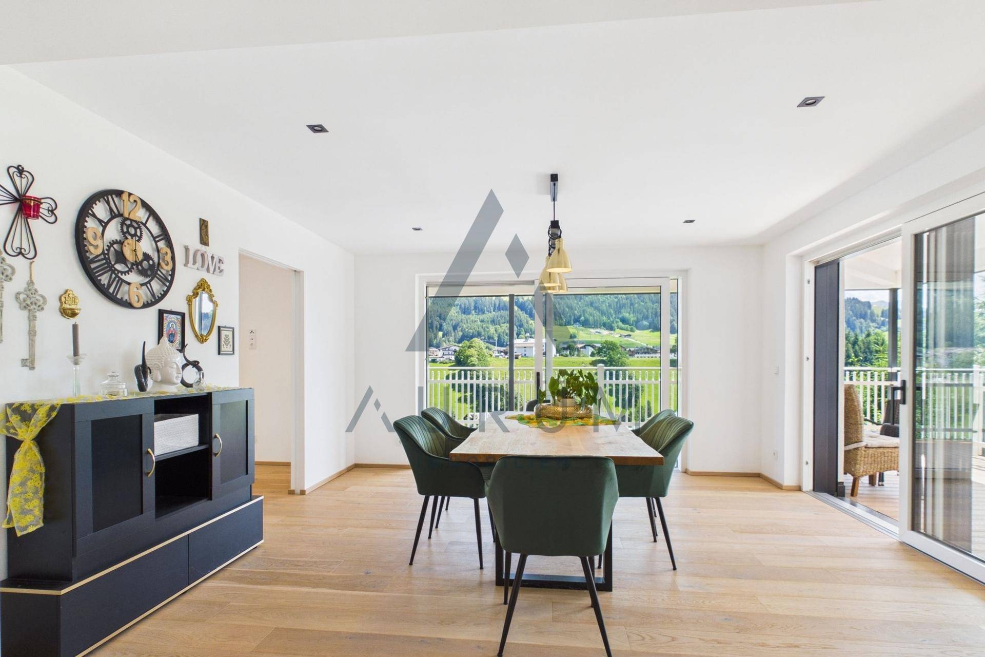 Heller Essbereich mit Holztisch, grünen Stühlen und Zugang zu einem Balkon mit Bergblick.