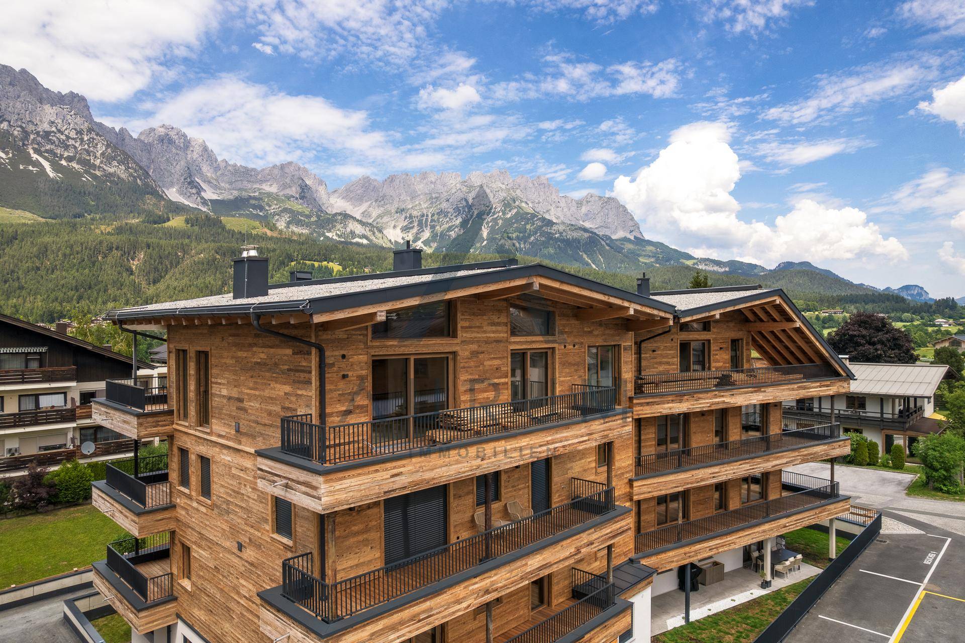 Modernes Holzgebäude mit mehreren Balkonen und Bergblick unter blauem Himmel.