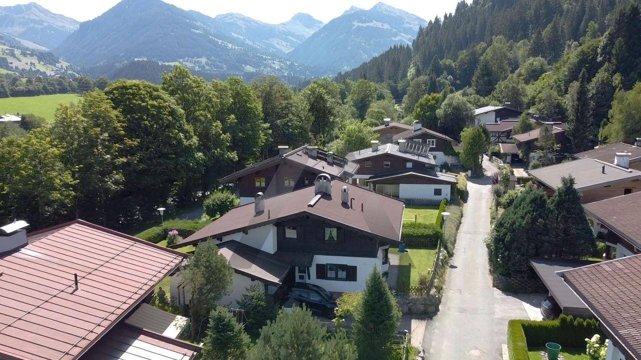 Weitläufige Luftaufnahme einer Wohnsiedlung in den Alpen mit vielen Bäumen und beeindruckendem Bergpanorama.