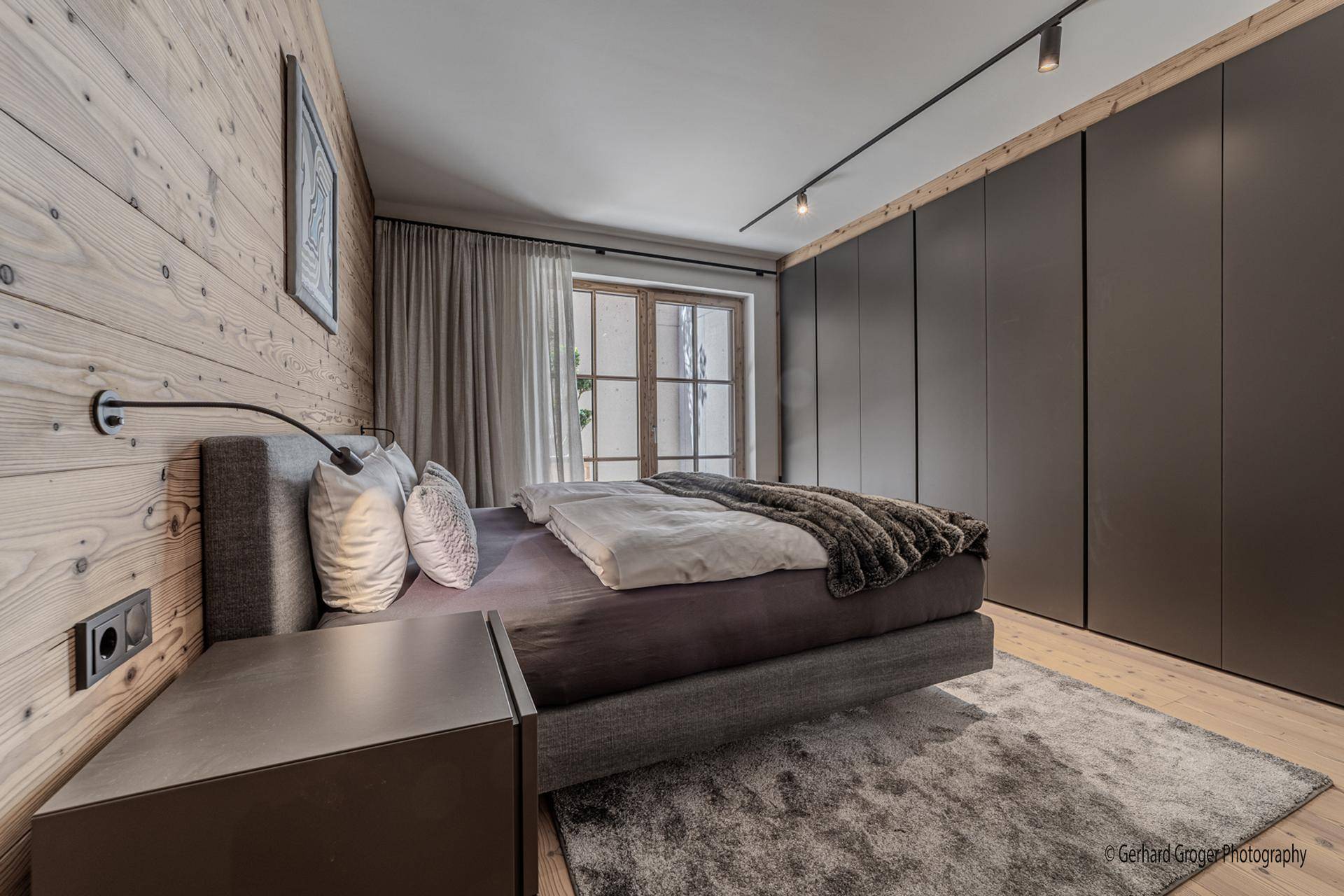 Gemütliches Schlafzimmer mit Holzwänden, Einbauschränken und Zugang zu einem Außenbereich.
