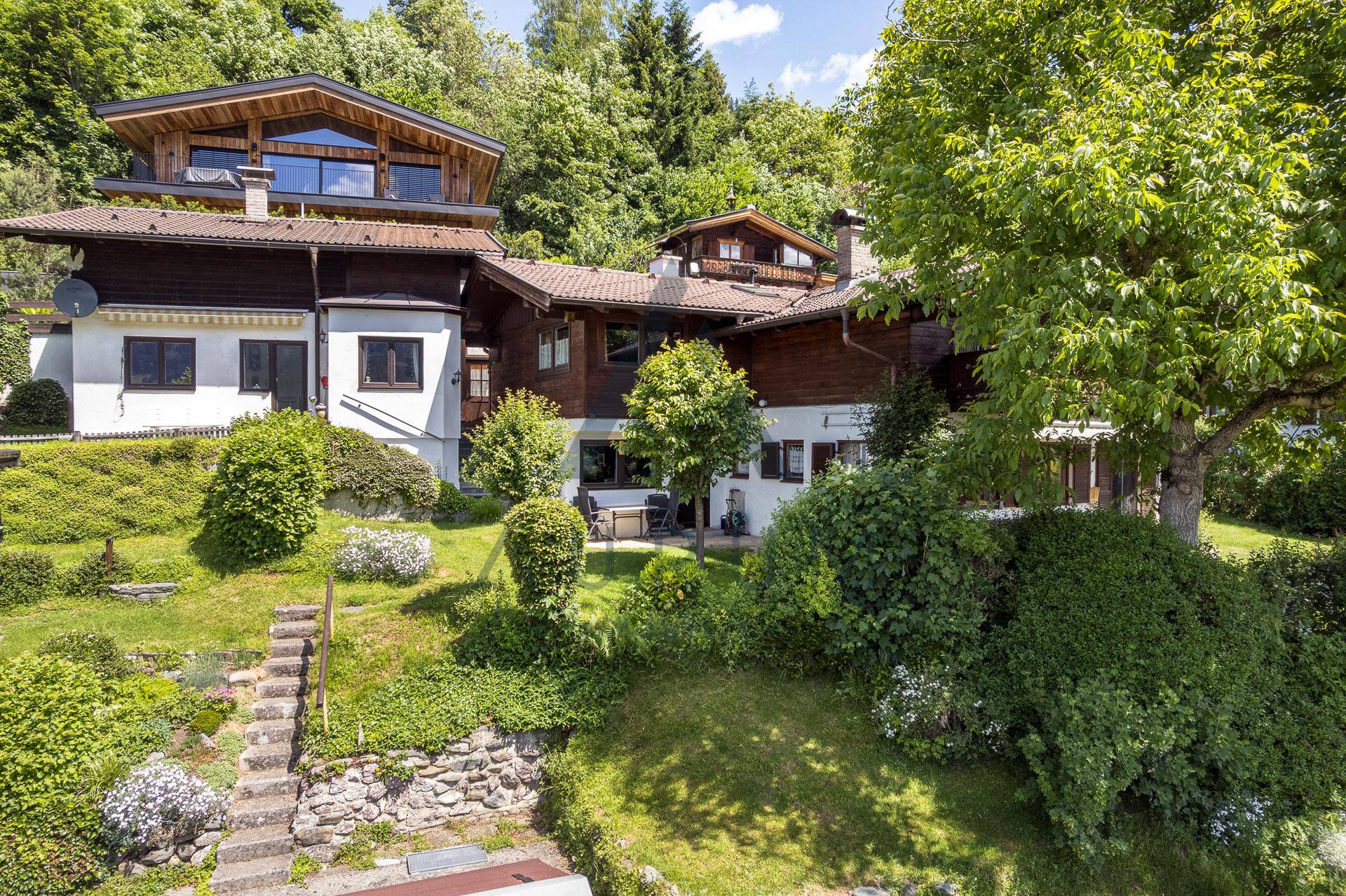Weitläufiger Garten mit altem Baumbestand und einem traditionellen Haus im Hintergrund.