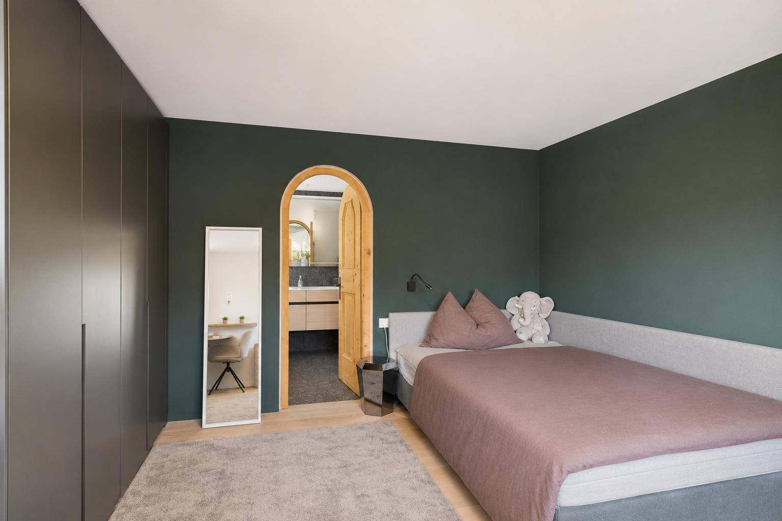 Modernes Schlafzimmer mit dunkelgrüner Wand, Einbauschränken und Zugang zu einem Badezimmer.