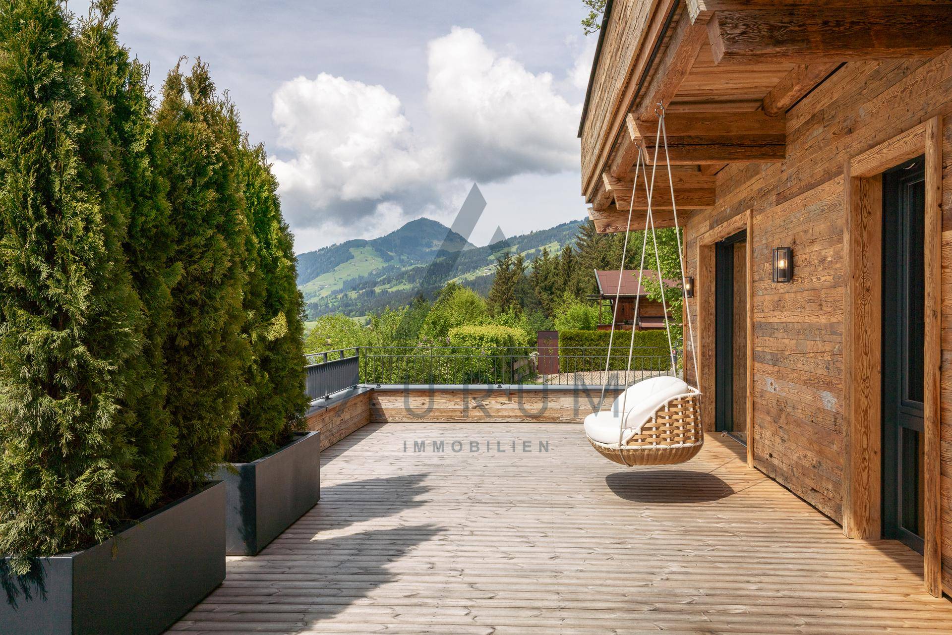 Weitläufige Holzterrasse mit Hängesessel und Panoramablick auf die umliegende Berglandschaft.