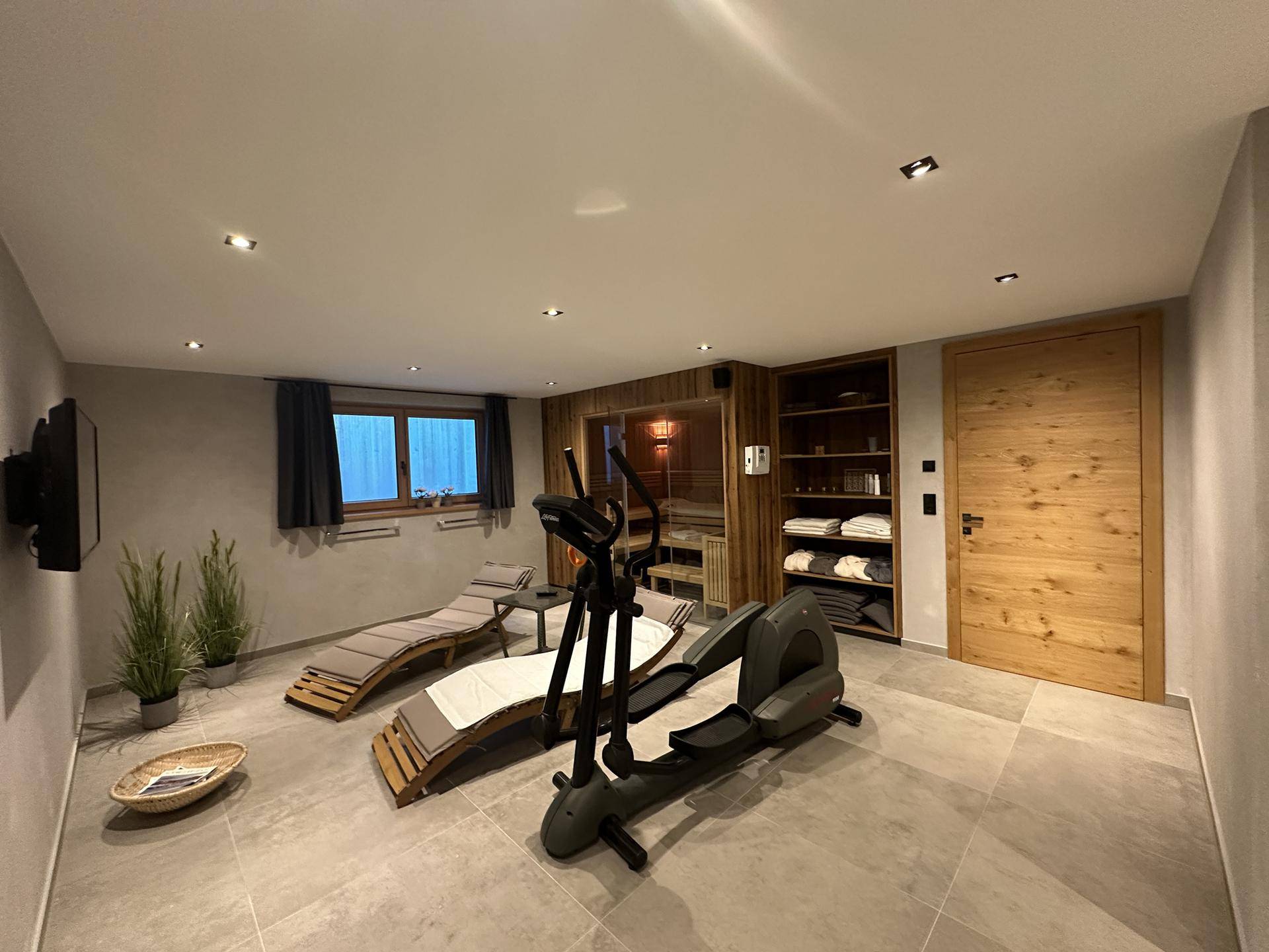 Wellnessbereich mit Sauna, Fitnessgeräten und Liegestühlen zur Entspannung.