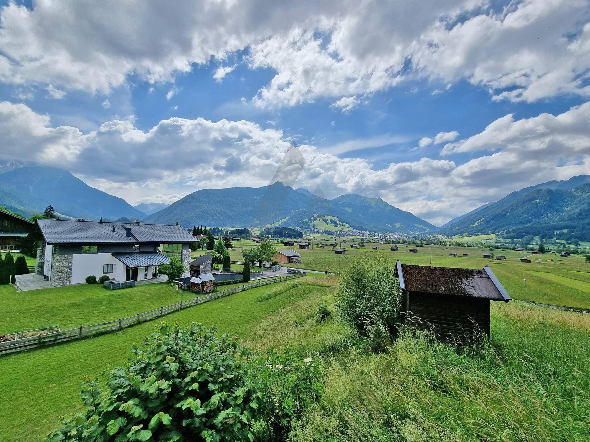 Weitläufige Landschaft mit einem modernen Wohnhaus, einem kleinen Schuppen und beeindruckendem Bergblick.