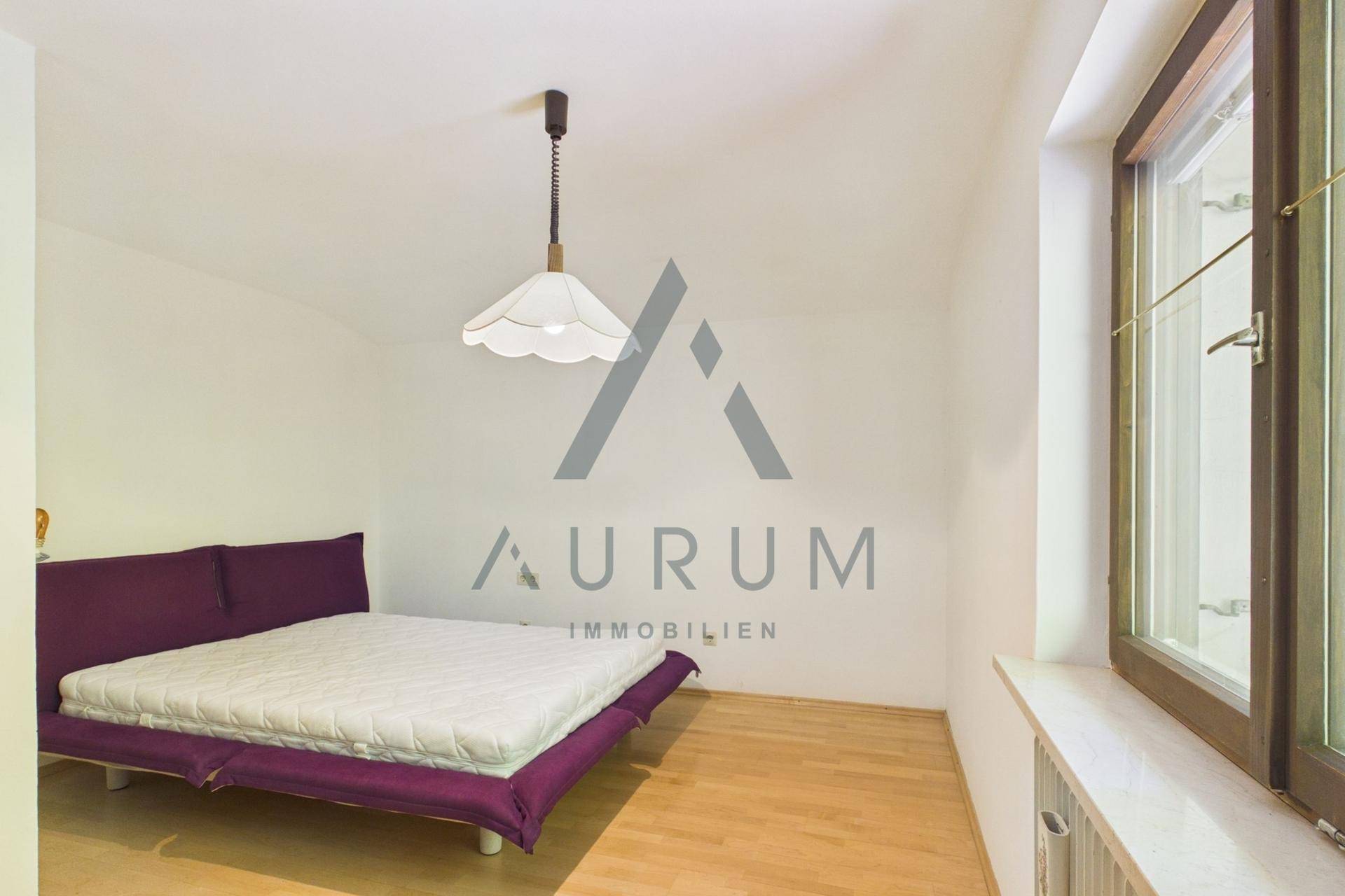 Einfaches Schlafzimmer mit Holzboden, großem Fenster und lila Bett.