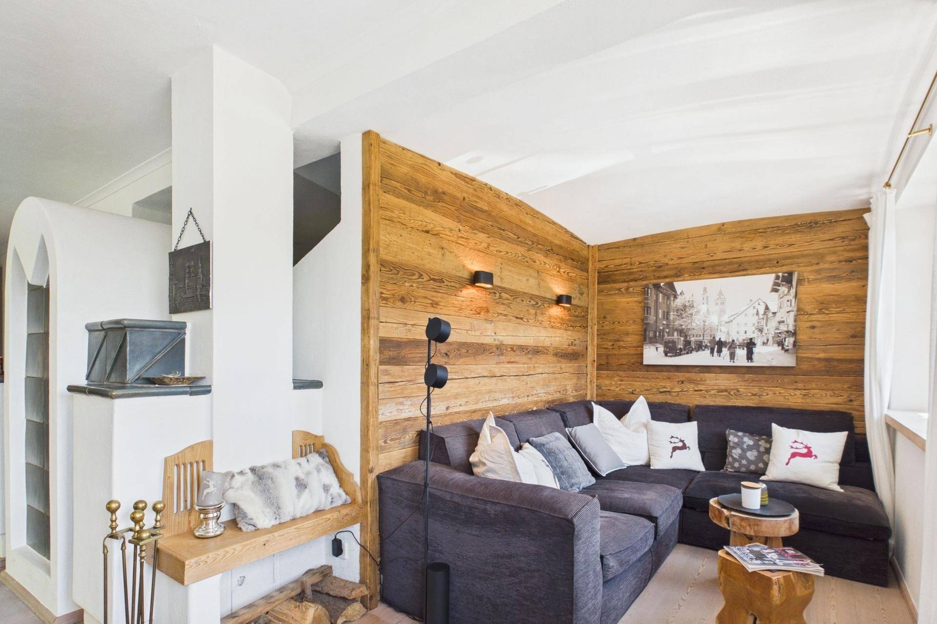 Gemütliches Wohnzimmer mit Holzwänden, großem Sofa und einem traditionellen Kachelofen.