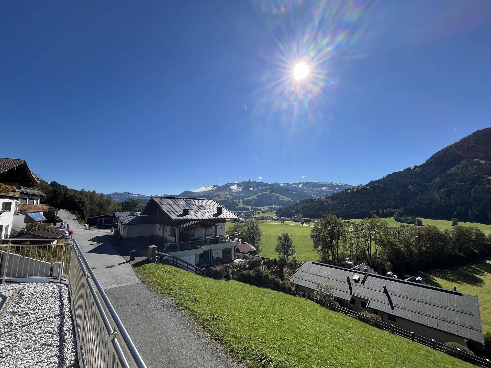 Panoramablick auf die ländliche Umgebung mit Häusern, einer Straße und schneebedeckten Bergen am Horizont.