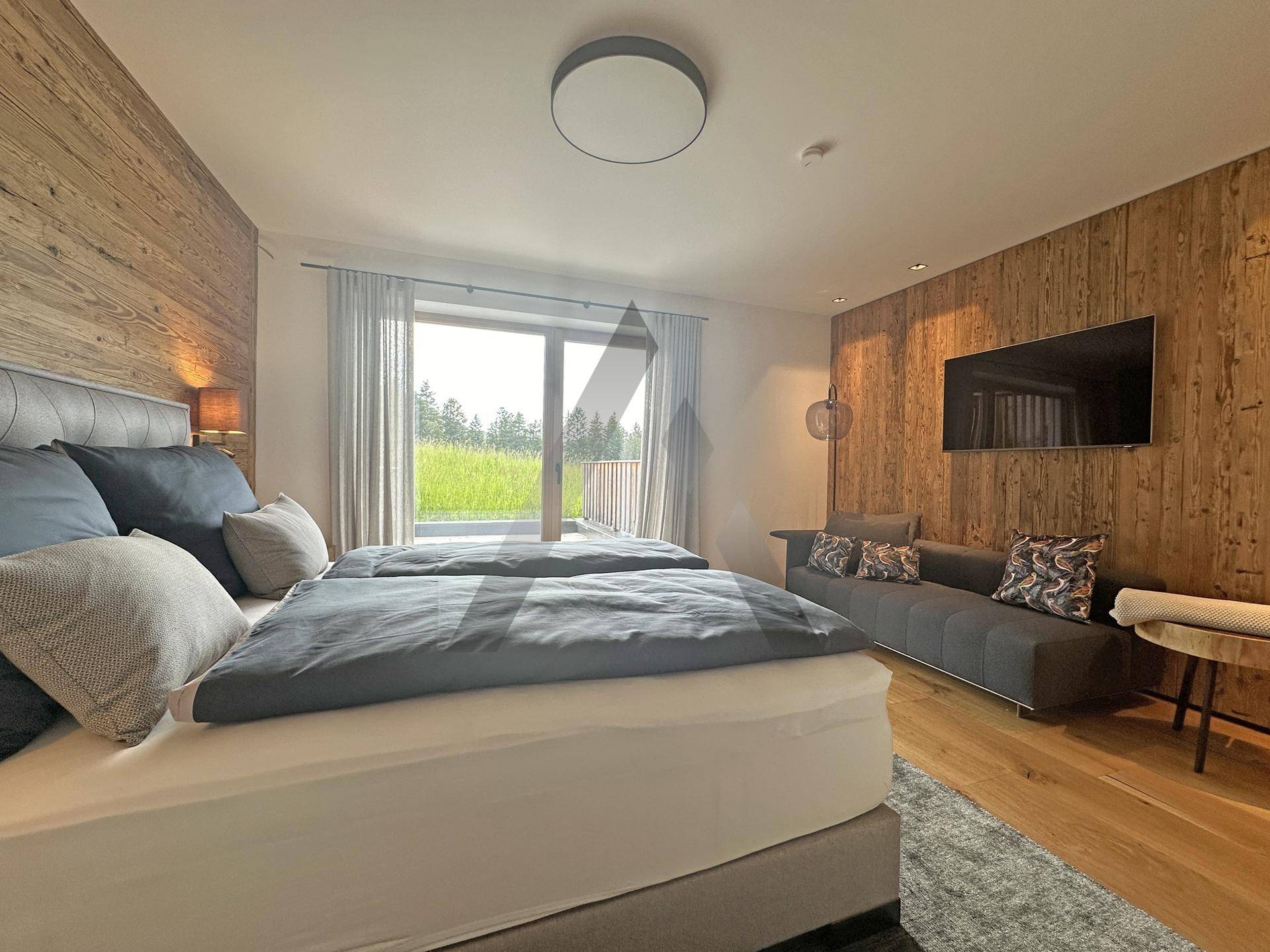 Komfortables Schlafzimmer mit Holzwänden, Doppelbett und Zugang zum Balkon mit Grünblick.