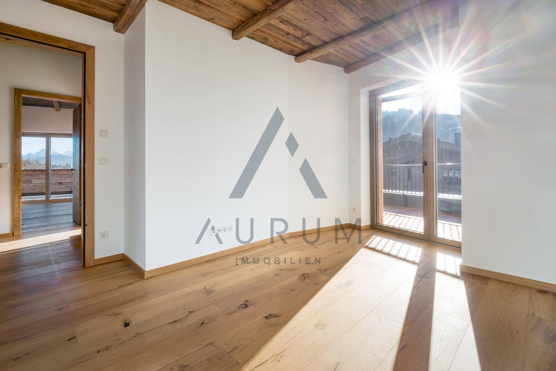 Sonniges Zimmer mit Holzboden und direktem Zugang zu einem Balkon oder einer Terrasse.