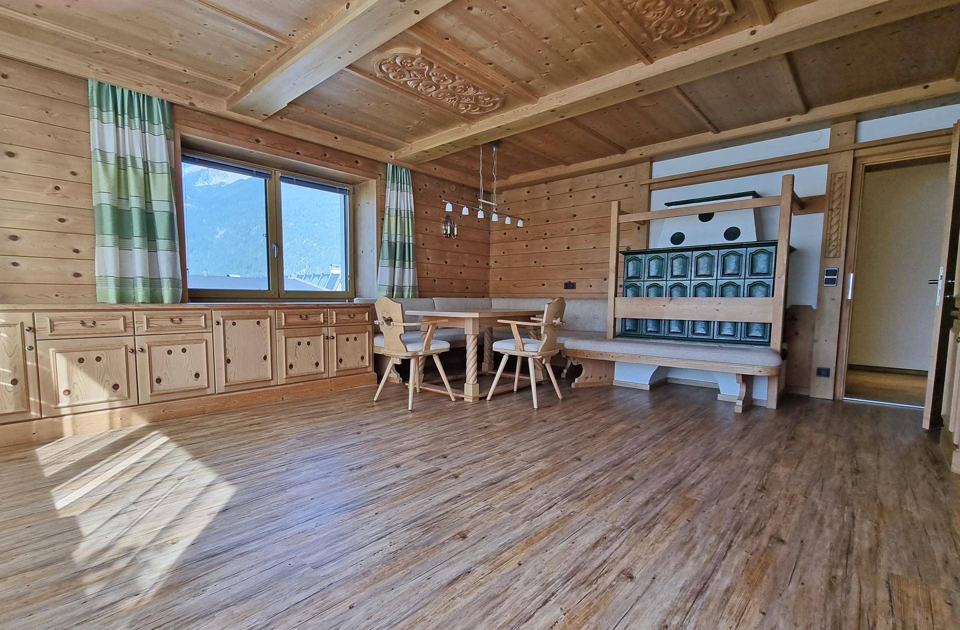 Gemütlicher alpiner Wohnbereich mit Holztäfelung, Kachelofen und Essbereich.
