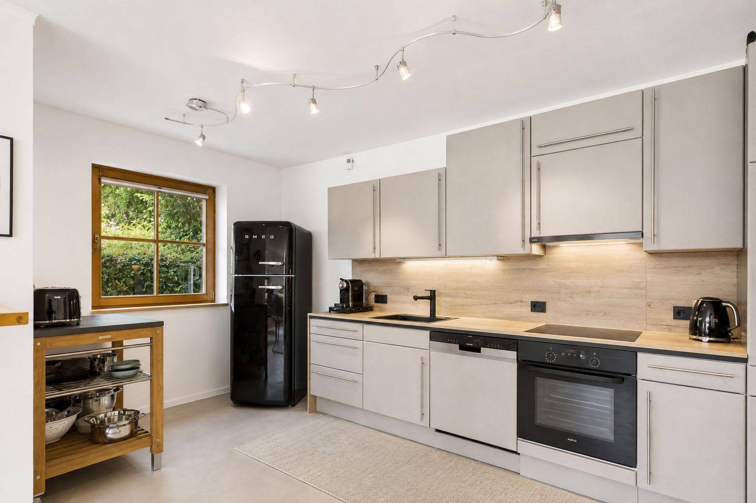 Moderne Küche mit hellgrauen Schränken, Holzarbeitsplatten und einem schwarzen Retro-Kühlschrank.