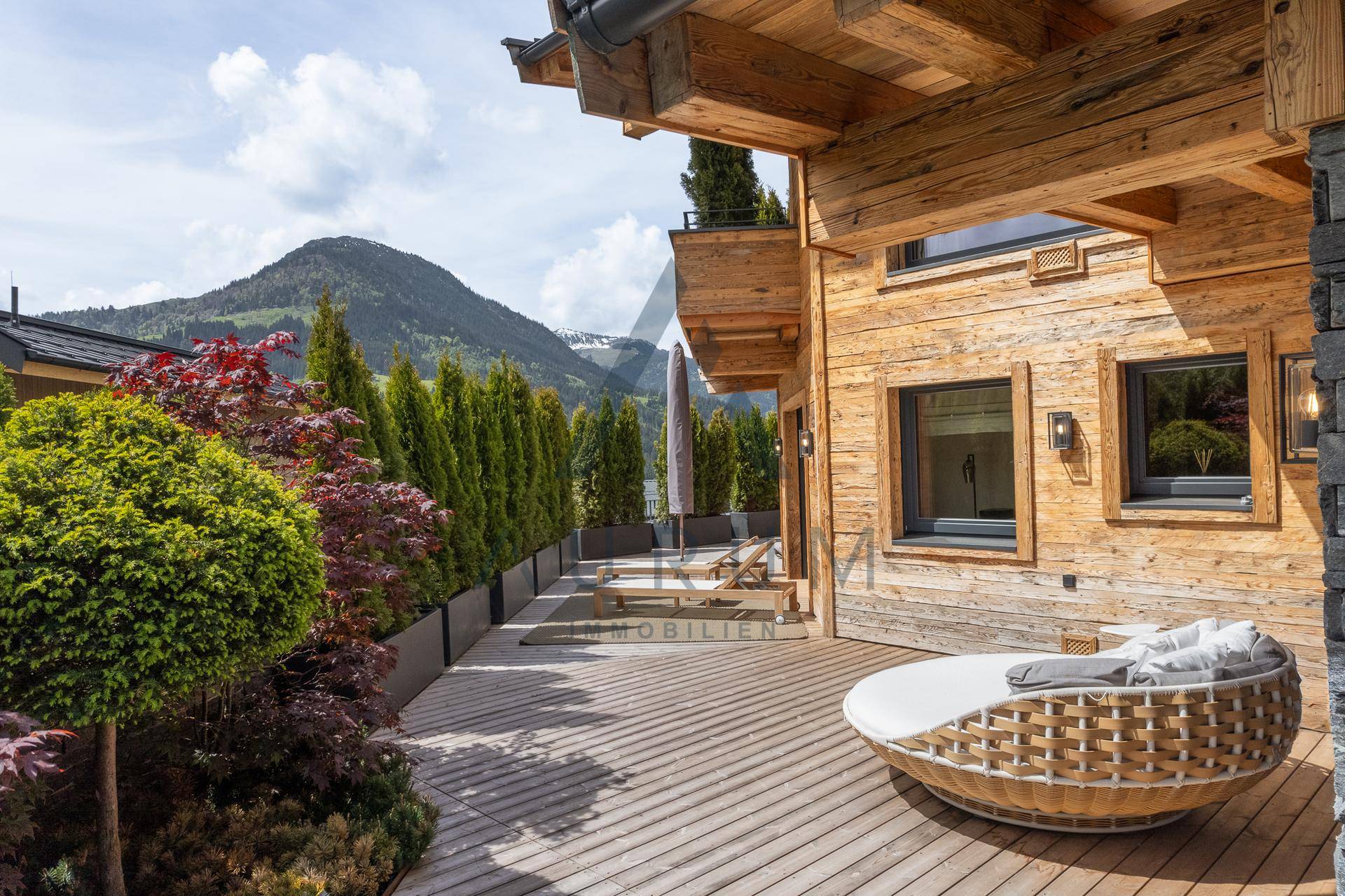 Geräumige Holzterrasse mit bequemer Liege und atemberaubendem Bergblick in sonniger Lage.