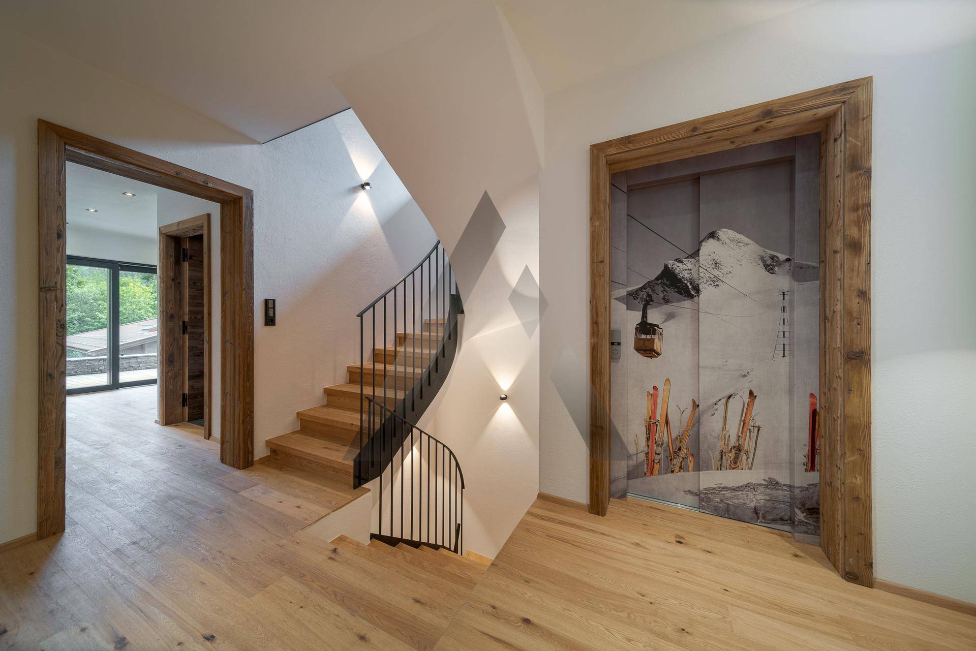 Heller Flur mit Holztreppe, schmiedeeisernem Geländer und Holzböden, modern und einladend.