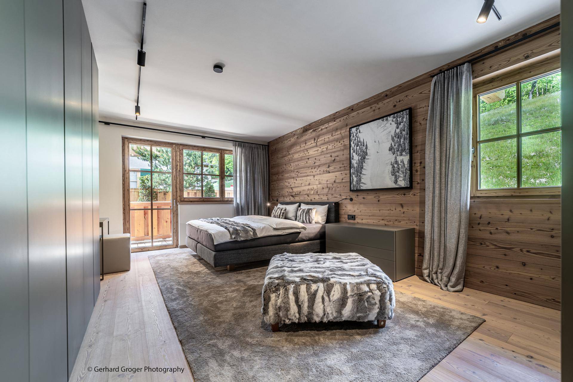 Modernes Schlafzimmer mit Holzwand, großem Bett und Zugang zu einem Balkon mit Bergblick.