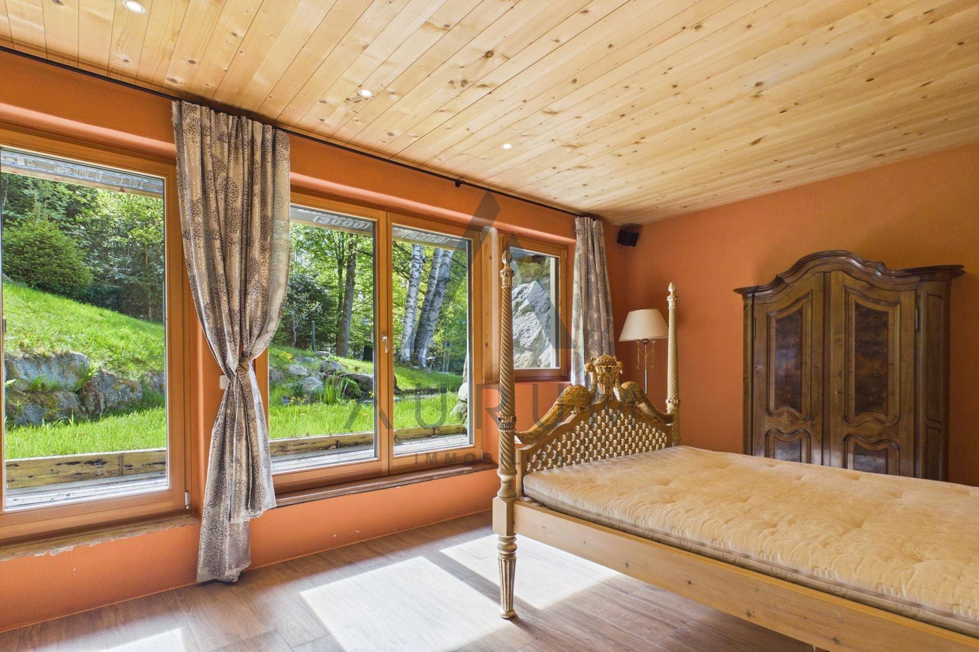 Helles Schlafzimmer mit Holzboden und großen Fenstern mit Ausblick auf den Garten und Teich.